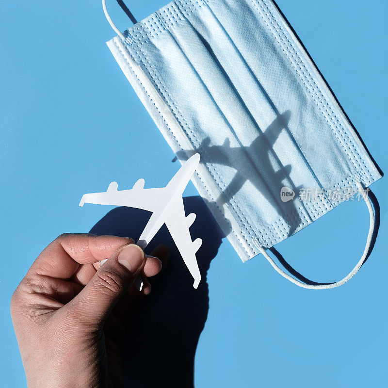 封锁后的空中旅行手持纸飞机飞过医用口罩，从阴影到光亮。通过Covid - 19大流行恢复国内和国际旅行。电晕对航空的影响